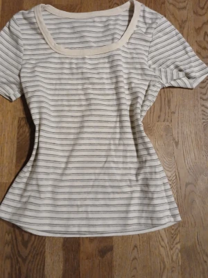 Tight t-shirt - Säljer en vit t-shirt med tunna svarta ränder och rundad halsringning. T-shirten har korta ärmar och en mjuk, bekväm passform. Perfekt till jeans eller kjol för en enkel och stilren look.