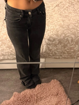 Svarta raka jeans med låg midja - Säljer ett par svarta low waisted jeans med raka ben från Lager 157 i strl XXS. Jeansen har klassisk femficksdesign och silverfärgade knappar. Materialet är denim med en lätt tvättad look som ger en cool vibe. Perfekta till en avslappnad stil.