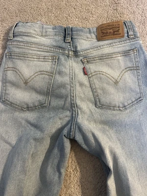 Ljusblå Levi's jeans lowwaist wide - Säljer ett par ljusblå Levi's jeans i klassisk femficksmodell. Jeansen har raka ben, slitningar på vänster lår och den ikoniska läderlappen bak i midjan. Tillverkade i bomull med en avslappnad passform och snygga detaljer som kontrastsömmar och röd Levi's-tag.