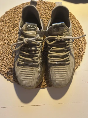 Beige sneakers från Steve Madden - Snygga beige sneakers från Steve Madden med stickad ovandel och transparent sula. Skorna har coola detaljer med svarta och silvriga stenar på sidan samt textdetaljer vid hälen. Perfekta för dig som gillar streetstyle och vill sticka ut.