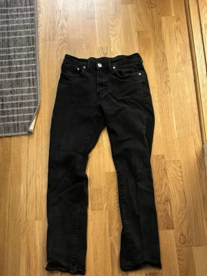 Svarta raka jeans - Säljer ett par svarta jeans med rak passform och klassisk femficksdesign. Jeansen har normal midja och stängs med knapp och dragkedja. Materialet ser ut att vara bomull med lite stretch för extra komfort.