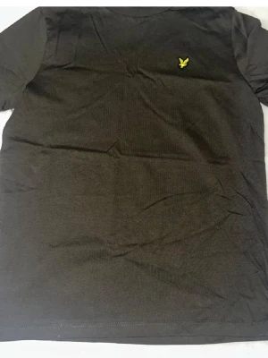 Mörkblå t-shirt från Lyle & Scott - En stilren mörkblå t-shirt från Lyle & Scott med klassisk passform och korta ärmar. T-shirten har en gul broderad logotyp på bröstet och är tillverkad i mjuk bomull som känns skön mot huden. Perfekt till jeans eller shorts.
