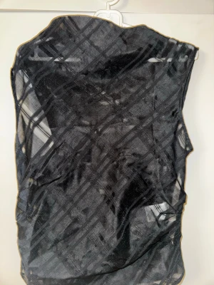 Svart mesh topp från Bik Bok - Säljer en svart transparent mesh topp från Bik Bok med rutigt mönster. Toppen är ärmlös och har en lätt glittrig finish samt snörning i sidan för en cool detalj. Perfekt att styla lager på lager för en trendig look.