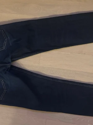 Mörkblå raka jeans - Säljer ett par mörkblå jeans med raka ben och klassiska bakfickor. Jeansen har kontrastsömmar och är tillverkade i ett mjukt denimtyg som sitter snyggt. Perfekta för dig som gillar en enkel och stilren look.