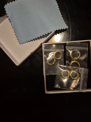 3-pack guldpläterade huggie hoops - Säljer ett 3-pack huggie hoops i 18K guldpläterat 925 silver. Två par är släta och ett par är dekorerade med gnistrande stenar. Alla är små, runda och passar perfekt att stapla. Hypoallergena och bekväma att bära.