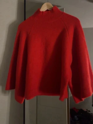 Röd stickad polotröja - Säljer en snygg röd stickad polotröja med hög krage och avslappnad passform. Tröjan har trekvarts ärmar och är gjord i ett mjukt, värmande material. Perfekt för kyliga dagar och enkel att styla till olika outfits.