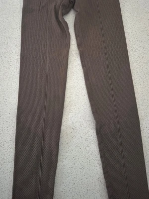 Bruna texturerade träning byxor - Säljer två par bruna tränings byxor med hög midja och snyggt texturerat mönster. De är stretchiga och sitter tight, perfekta till en avslappnad eller sportig look. Materialet är mjukt och följsamt för extra komfort.