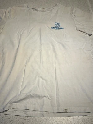Vit t-shirt Barcelona Wituka - Vit t-shirt från Wituka med blå Barcelona-tryck på bröstet. Klassisk rund hals och korta ärmar. Tillverkad i mjuk bomull som känns skön mot huden. Perfekt för dig som gillar enkel och stilren design med en twist.