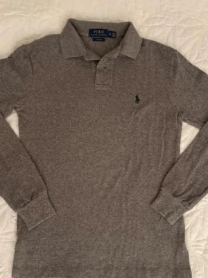 Grå långärmad piké från Polo Ralph Lauren - Snygg grå långärmad piké från Ralph lauren, storlek XS. Skick 9/10 (inget fel på den) skriv vid frågor. Perfekt för sommaren