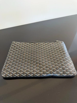 Goy datorfodral - Snyggt datorfodral från Goy i klassiskt svart och grått monogrammönster. Fodralet är tillverkat i slitstarkt canvasmaterial och har dragkedja upptill. Perfekt för att hålla din laptop skyddad och stilren när du är på språng.