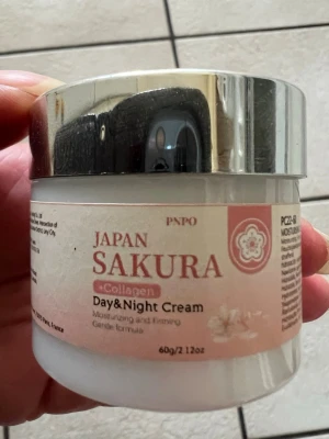 Japan Sakura Collagen Day & Night Cream 60 g - Fuktgivande dag- och nattkräm med kollagen från Japan Sakura. Kommer i en rund, vit burk med silverfärgat lock och rosa etikett. Krämen är framtagen för att återfukta och ge fastare hud med en mild formula. Innehåller 60g.