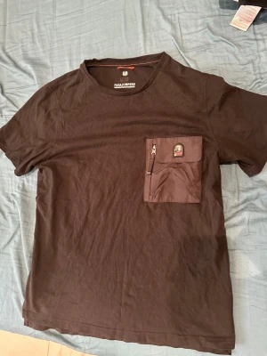 Svart t-shirt från Parajumpers - Säljer en svart t-shirt från Parajumpers med en unik bröstficka som har dragkedja och patch med logga. T-shirten har rund hals och korta ärmar. Perfekt för dig som gillar stilrena plagg med coola detaljer.