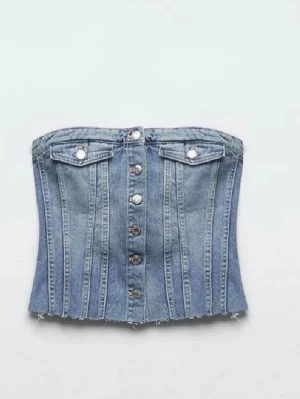 Blå jeanskorsett med knappar - Trendig blå jeanskorsett med knappar framtill och två dekorativa bröstfickor. Axelbandslös design och rå kant nertill ger en edgy vibe. Perfekt att styla med höga jeans eller kjol för en cool look.