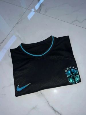 Svart Brasilien Nike fotbollströja - Snygg svart fotbollströja från Nike med Brasilien-emblem på bröstet och turkosa detaljer. Tröjan har rund halsringning och korta ärmar, samt diskret mönster i tyget. Perfekt för träning eller match.