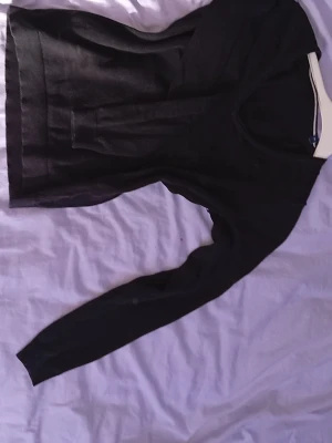 Svart stickad tröja från GANT - Svart stickad tröja från GANT med diskret broderad logga på bröstet. Tröjan har v-ringning och långa ärmar, perfekt för lager-på-lager. Klassisk och stilren design som passar till många olika outfits.