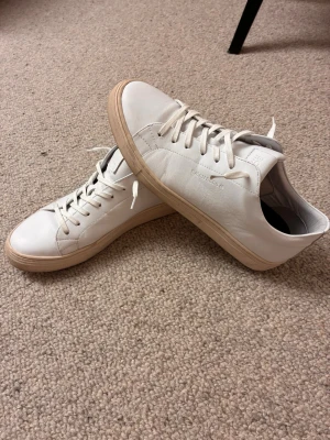 Vita sneakers från Björn Borg  - Stilrena vita sneakers från Björn Borg i slät läder med beige sula. Klassisk låg modell med vita skosnören och diskret logga på sidan. Perfekta för en clean och modern look.