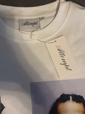 Lång sleeve från Attempt - Vit t-shirt från Attempt med stort tryck framtill som föreställer ett mugshot-porträtt och textdetaljer. Klassisk rund halsringning och rak passform. Perfekt för dig som gillar streetwear och unika prints.