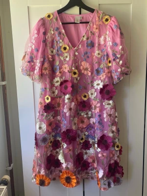 Rosa blommig klänning med puffärm - Superfin rosa klänning med broderade blommor i flera färger och puffärmar. Perfekt för sommarens alla tillfällen och ger en färgglad och lekfull look. Nypris:1800