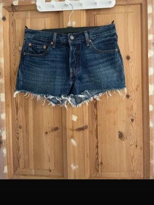 Levi's mörkblå jeansshorts frans - Säljer ett par mörkblå jeansshorts från Levi's med råa, fransiga kanter och klassisk femficksdesign. Shortsen har normal passform och är tillverkade i slitstark bomull. Perfekta för sommaren och ger en avslappnad vibe. Använda en gång 🤗