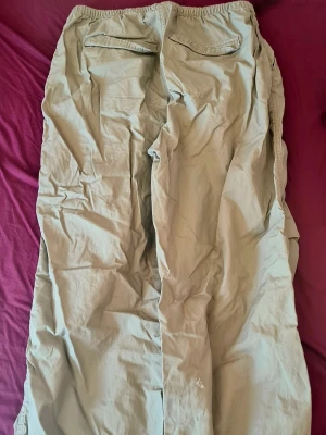 Beiga cargobyxor med resår - Säljer ett par beiga cargobyxor med avslappnad passform och resår i bensluten. Byxorna har flera fickor på sidorna och är tillverkade i ett lätt bomullsmaterial. Perfekta för en chill och street-inspirerad stil.