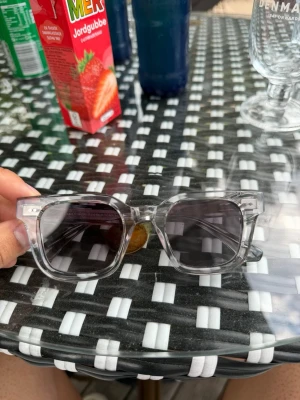 Transparenta solglasögon från Chimi - Snygga transparenta solglasögon från Chimi med klassisk fyrkantig form och mörka glas. Ramen är helt genomskinlig vilket ger en modern och clean look. Designade i Stockholm och perfekta för dig som vill ha en stilren accessoar. 45/24 i storlek 