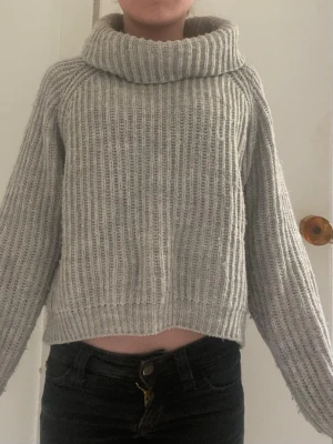Grå stickad polotröja - Mysig grå stickad polotröja med bred krage och avslappnad passform. Tröjan har ribbstickat mönster och långa ärmar, perfekt för kyliga dagar. Passar dig som gillar en enkel men snygg stil.
