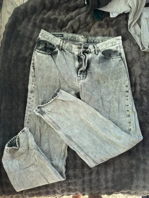Grå tvättade jeans från J.Lindeberg - Säljer ett par grå tvättade jeans från J.Lindeberg med klassisk femficksmodell och raka ben. Jeansen har en snygg vintagekänsla och är perfekta för en avslappnad streetstyle-look. Materialet är slitstarkt denim i bomull.