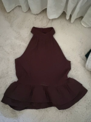 Mörklila ärmlös blus från Gina Tricot - Snygg mörklila blus från Gina Tricot i storlek XS. Blusen är ärmlös med hög hals och volang nedtill som ger en feminin siluett. Tillverkad i ett lätt, vävt material som känns luftigt och bekvämt. Perfekt att styla med jeans eller kjol.