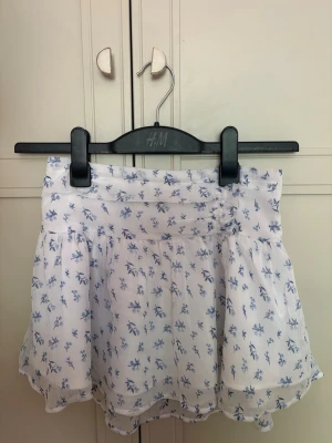 Vit kjol, detaljer-blå kjol🫰 Från gina Tricot💗 - Söt vit kortkjol från Gina med blått blommönster. Kjolen har volangkant och är tillverkad i ett lätt och luftigt material, perfekt för varma dagar. Resår i midjan för skön passform och flowig känsla.