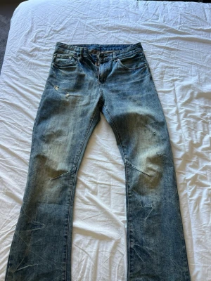 Blå slitna jeans med straight passform - Säljer ett par blå jeans med slitningar och raka ben. Jeansen har klassisk femficksmodell och ljus tvätt med tydliga slitningar på låren och knäna.