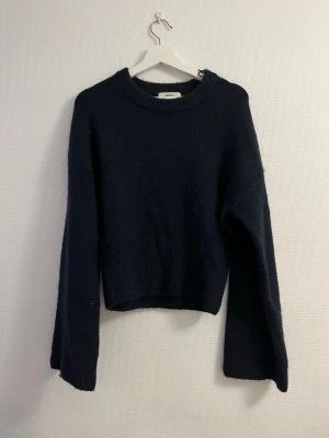 Mörkblå stickad tröja - Mysig mörkblå stickad tröja med rund halsringning och långa ärmar. Tröjan har en enkel, rak passform och bred ribbstickad kant nedtill samt vid ärmsluten. Perfekt för kyliga dagar och enkel att matcha med olika outfits.