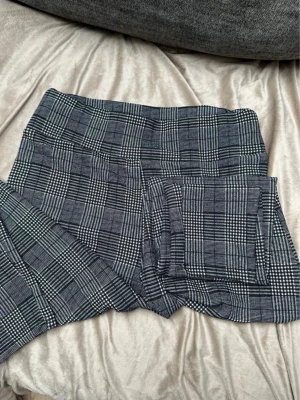 Gråa rutiga byxor med hög midja - Snygga gråa byxor med rutigt mönster och hög midja. Klassisk passform och stilren look som passar till många olika outfits. Materialet känns mjukt och stretchigt, troligen en blandning av polyester och bomull.