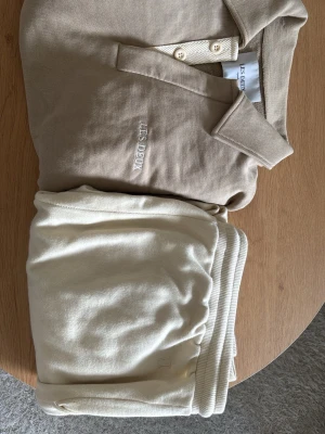 Beige pikétröja från Les Deux - Klassisk beige pikétröja från Les Deux med krage och knappar framtill. Tröjan har diskret broderad logga på bröstet och är tillverkad i mjuk bomull. 