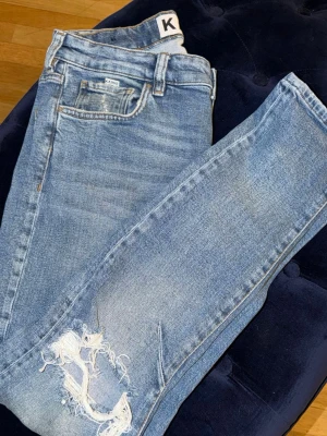 Blå slitna jeans från KANVY - Snygga ljusblå jeans från KANVY med slitningar på ena knät och klassisk femficksdesign. Jeansen har en smal passform och är tillverkade i denim med stretch för extra komfort. Perfekta för en avslappnad och trendig look.
