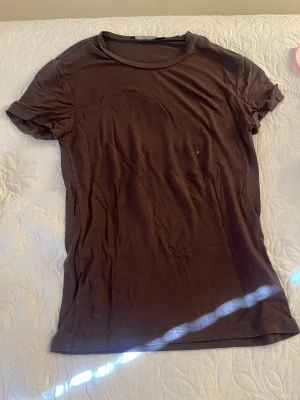 Brun basic t-shirt i bomull - En enkel brun t-shirt med rund hals och korta ärmar. Tillverkad i mjuk bomull och har en klassisk passform som funkar till det mesta. Perfekt att matcha med jeans eller shorts för en avslappnad look.
