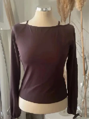 Mörkbrun långärmad topp - Snygg mörkbrun långärmad topp med smal passform och rund halsringning. Tillverkad i ett mjukt och stretchigt material som sitter bekvämt på kroppen. Perfekt att styla med jeans eller kjol för en trendig look. Sprung i armen 