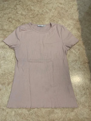 Ljusrosa ribbad t-shirt - Säljer en ljusrosa ribbad t-shirt från Kappahl. T-shirten har rund halsringning, korta ärmar och är tillverkad i mjuk bomullsmix. Enkel och stilren modell som passar perfekt till jeans eller kjol.