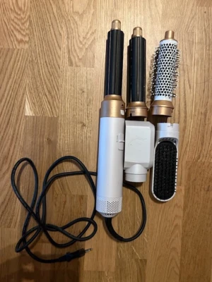 Multistyler för hår med tillbehör - Säljer en multistyler för hår i vitt och guld med tre utbytbara tillbehör: rundborste, locktång och borste. Perfekt för att fixa olika frisyrer hemma. Elektrisk med sladd och enkel att använda. Passar dig som gillar att experimentera med håret.