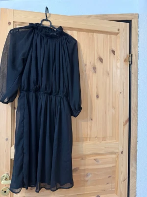 Svart chiffongklänning - Svart klänning i luftig chiffong med resår i midjan och trekvartsärmar. Klänningen har en rundad halsringning med lätt rynk och faller snyggt till knälängd. 