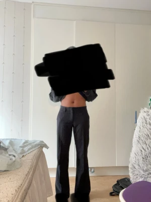 Svarta utsvängda kostymbyxor - Säljer ett par svarta kostymbyxor med utsvängda ben och hög/låg midja. Byxorna har en klassisk, stilren look och är perfekta för dig som gillar en trendig siluet Jag är 162cm och omkretsen runt mina lår är 51