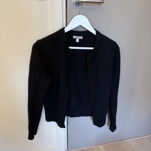 Svart kofta med rund hals - En enkel och stilren svart kofta från hm med rund hals och knäppning framtill. Koftan har långa ärmar och ribbade muddar vid ärmslut och nederkant. Perfekt att slänga över en t-shirt eller linne för en clean look. Köpte second hand men fortfarande bra kvalité! 