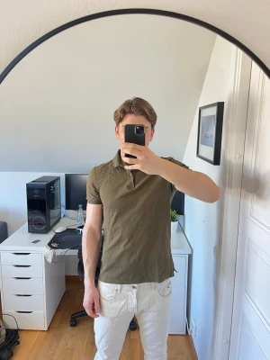 Olivgrön pikétröja från J.Lindberg  - Säljer en olivgrön pikétröja ifrån J.Lindberg med klassisk krage och knappar framtill. Den är gjord i 100% bomull. Hör gärna av dig vid frågor!