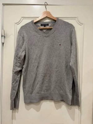 Grå V-ringad tröja Tommy Hilfiger - Klassisk grå V-ringad tröja från Tommy Hilfiger med liten broderad logga på bröstet. Den är egentligen i en mansmodell men har använt den själv. 