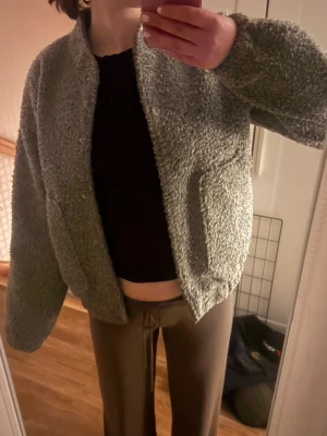 Grå teddyjacka med fickor - Mysig grå teddyjacka med knappar framtill och två stora fickor. Jackan har en avslappnad passform och är gjord i fluffigt teddy-material som håller dig varm. Har lite smink vid kragen 