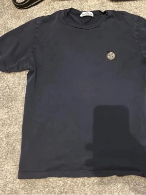 Mörkblå Stone Island t-shirt - Snygg mörkblå t-shirt från Stone Island med klassisk logopatch på bröstet. T-shirten har rund hals och korta ärmar, perfekt för en clean och stilren look. Tillverkad i mjuk bomull som känns skön mot huden. Lite mörkare nyans i verkligheten