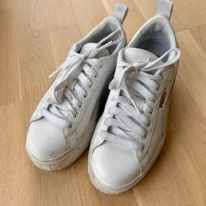 Vita Puma sneakers med platåsula - Stilrena vita sneakers från Puma med chunky platåsula och klassisk snörning. Skorna har diskret Puma-logga i guld på sidan och är tillverkade i slätt lädermaterial. Perfekta för dig som gillar en clean och sportig look.
