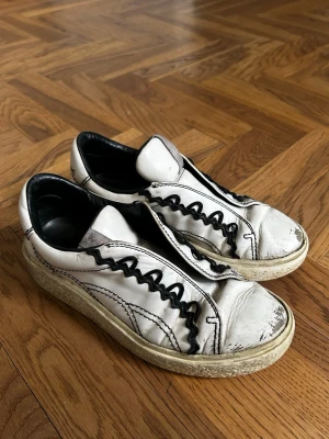 See By Chloe Sneakers *37* - Unika vita sneakers med svarta vågiga snören och chunky sula. Skorna har en retroinspirerad look med kontrasterande detaljer och bred plös. Tillverkade i läder med svart innerfoder och slitna detaljer för en cool, avslappnad stil.