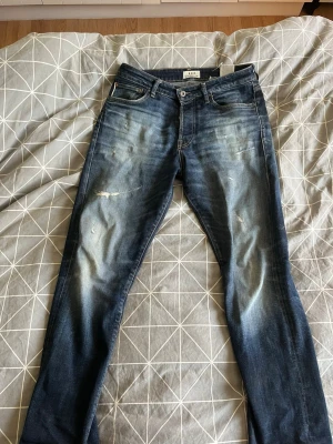 Royal denim decision blå slitna jeans herr - Säljer ett par blå jeans med slitningar och tvättade detaljer. Klassisk femficksmodell med knappgylf och raka ben. Jeansen har en snygg faded effekt och patch bak i midjan. Perfekta för en avslappnad och trendig look. Tyvärr har den hål i fickan som går att lösa annars fint skick!