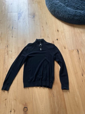 Svart halvzip-tröja Jack & Jones - Snygg svart långärmad tröja från Jack & Jones med halvzip och hög krage. Tillverkad i mjukt stickat material som ger en clean look. Perfekt till jeans eller chinos för en stilren outfit.