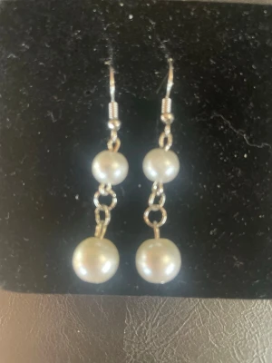 Silvriga örhängen med vita pärlor - Säljer ett par eleganta örhängen med två vita pärlor på varje örhänge. De har en droppformad design med metall i silverfärg och klassisk krok. Perfekta för dig som gillar stilrena accessoarer med pärldetaljer.